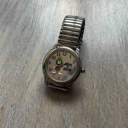 Warner Bros Marvin the Martian 1996 Analog Watch is a stainless steel watch with a shiny finish and a stretch expansion bracelet made from connected metal links. The dial is metallic and reflective with blue numerals and a graphic of Marvin the Martian standing with his name printed beside him. The caseback includes Warner Bros 1996 licensing.