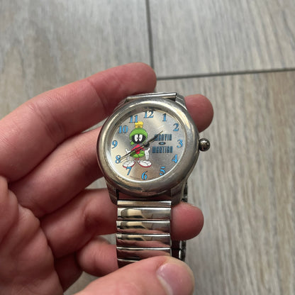 Warner Bros Marvin the Martian 1996 Analog Watch is a stainless steel watch with a shiny finish and a stretch expansion bracelet made from connected metal links. The dial is metallic and reflective with blue numerals and a graphic of Marvin the Martian standing with his name printed beside him. The caseback includes Warner Bros 1996 licensing.