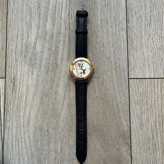 Warner Bros Sylvester 1990 Analog Watch features a gold-tone case with a white dial and black leather strap marked as genuine leather. The dial displays Sylvester with vertical “Sylvester” text, along with hour markers at 12, 3, 6, and 9. The watch uses a Japan movement and includes Warner Bros 1990 licensing engraved on the caseback