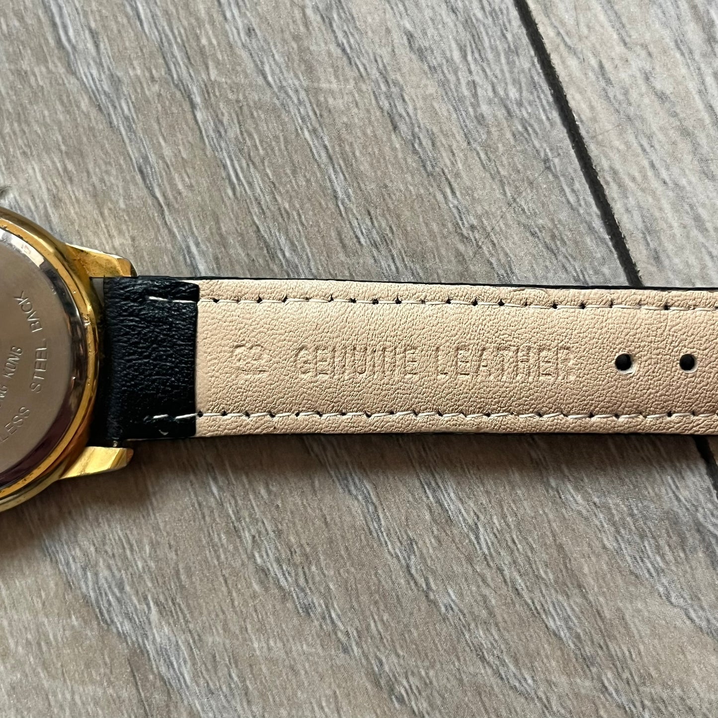 Warner Bros Sylvester 1990 Analog Watch features a gold-tone case with a white dial and black leather strap marked as genuine leather. The dial displays Sylvester with vertical “Sylvester” text, along with hour markers at 12, 3, 6, and 9. The watch uses a Japan movement and includes Warner Bros 1990 licensing engraved on the caseback