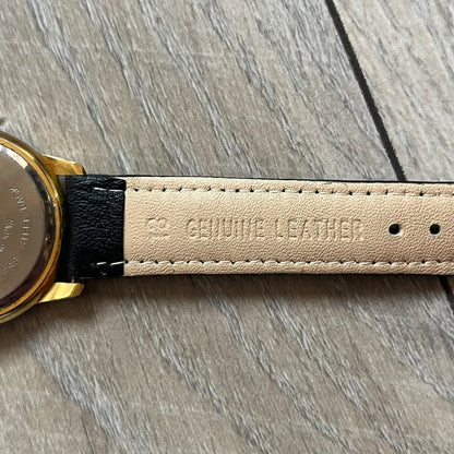 Warner Bros Sylvester 1990 Analog Watch features a gold-tone case with a white dial and black leather strap marked as genuine leather. The dial displays Sylvester with vertical “Sylvester” text, along with hour markers at 12, 3, 6, and 9. The watch uses a Japan movement and includes Warner Bros 1990 licensing engraved on the caseback