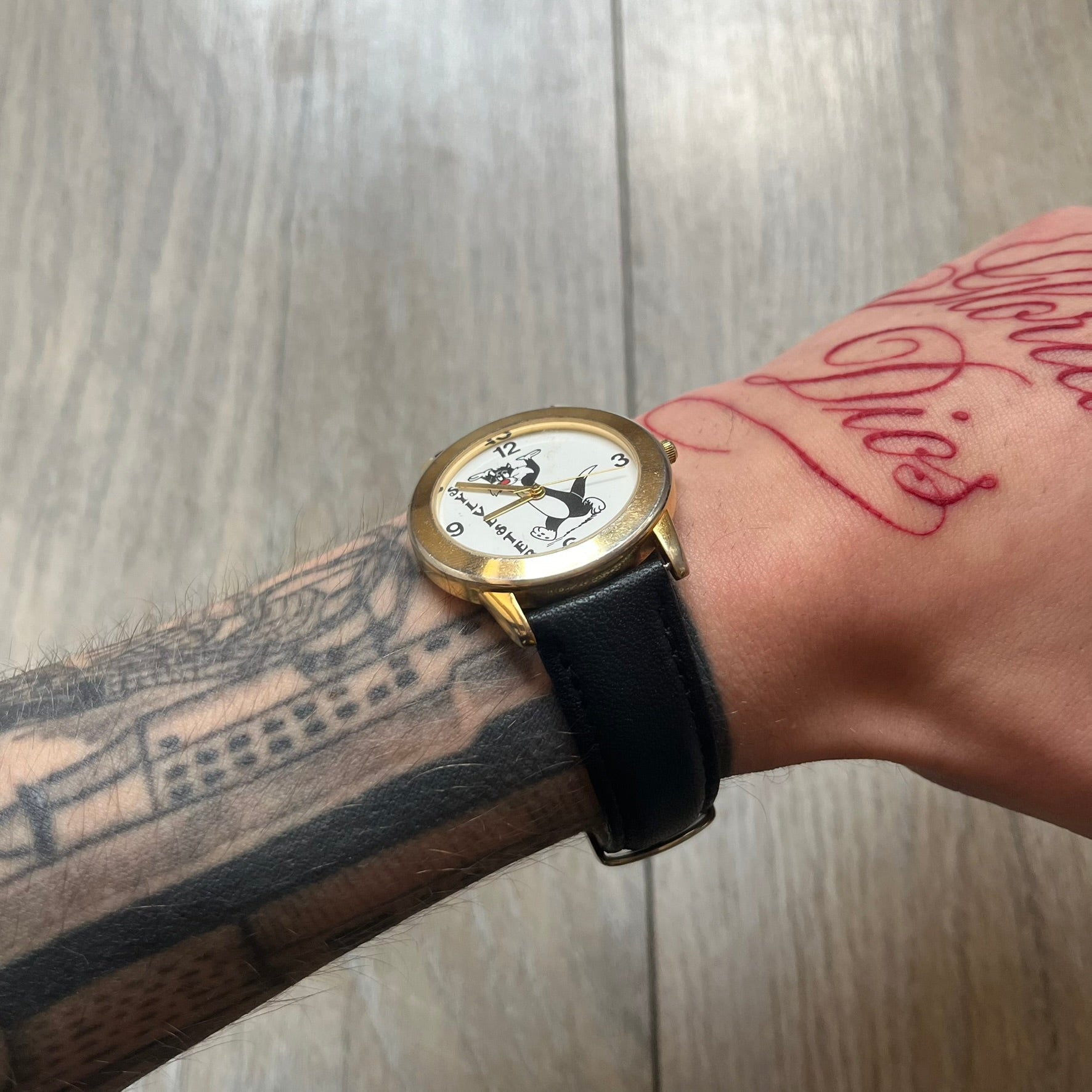 Warner Bros Sylvester 1990 Analog Watch features a gold-tone case with a white dial and black leather strap marked as genuine leather. The dial displays Sylvester with vertical “Sylvester” text, along with hour markers at 12, 3, 6, and 9. The watch uses a Japan movement and includes Warner Bros 1990 licensing engraved on the caseback