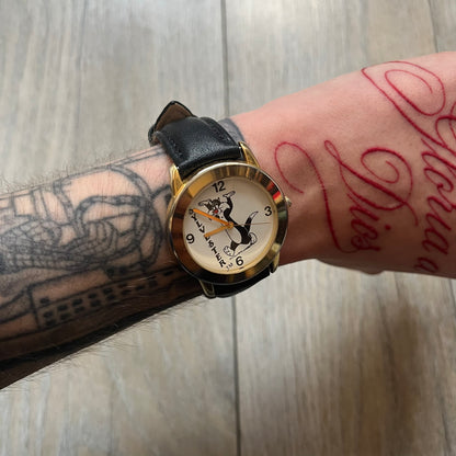 Warner Bros Sylvester 1990 Analog Watch features a gold-tone case with a white dial and black leather strap marked as genuine leather. The dial displays Sylvester with vertical “Sylvester” text, along with hour markers at 12, 3, 6, and 9. The watch uses a Japan movement and includes Warner Bros 1990 licensing engraved on the caseback