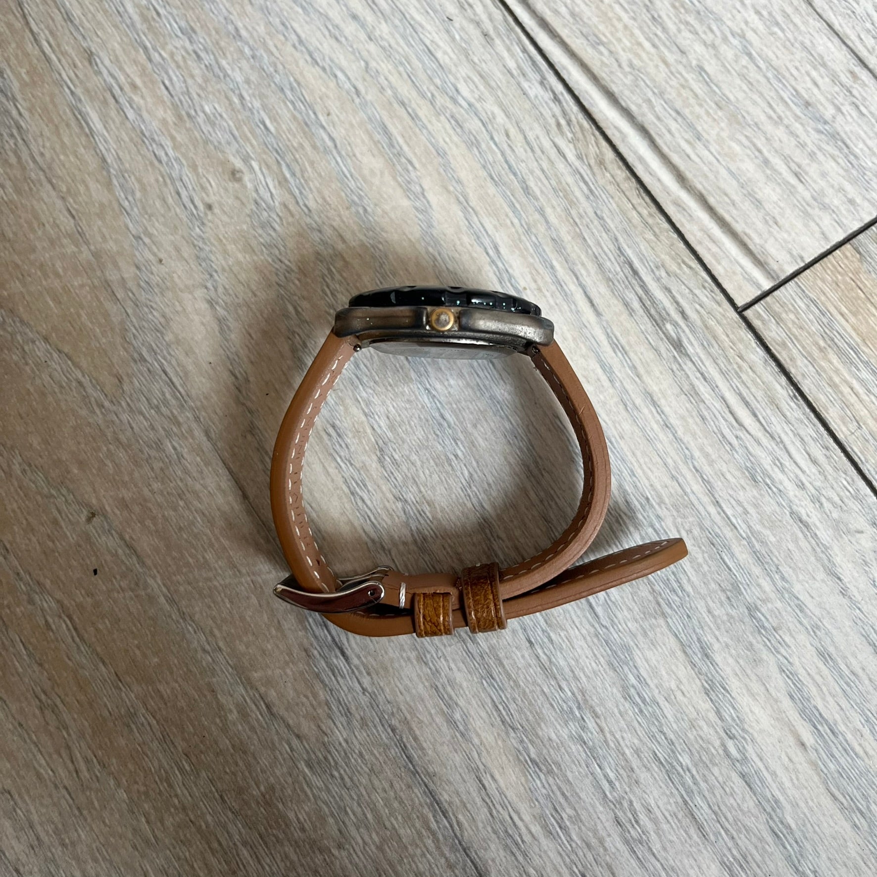 Warner Bros Tasmanian Devil 1997 Analog Watch is a stainless steel watch with a black-silver case and a fresh brown leather strap. The dial features a graphic of Taz smiling in front of a orange background. The caseback includes Warner Bros 1997 licensing