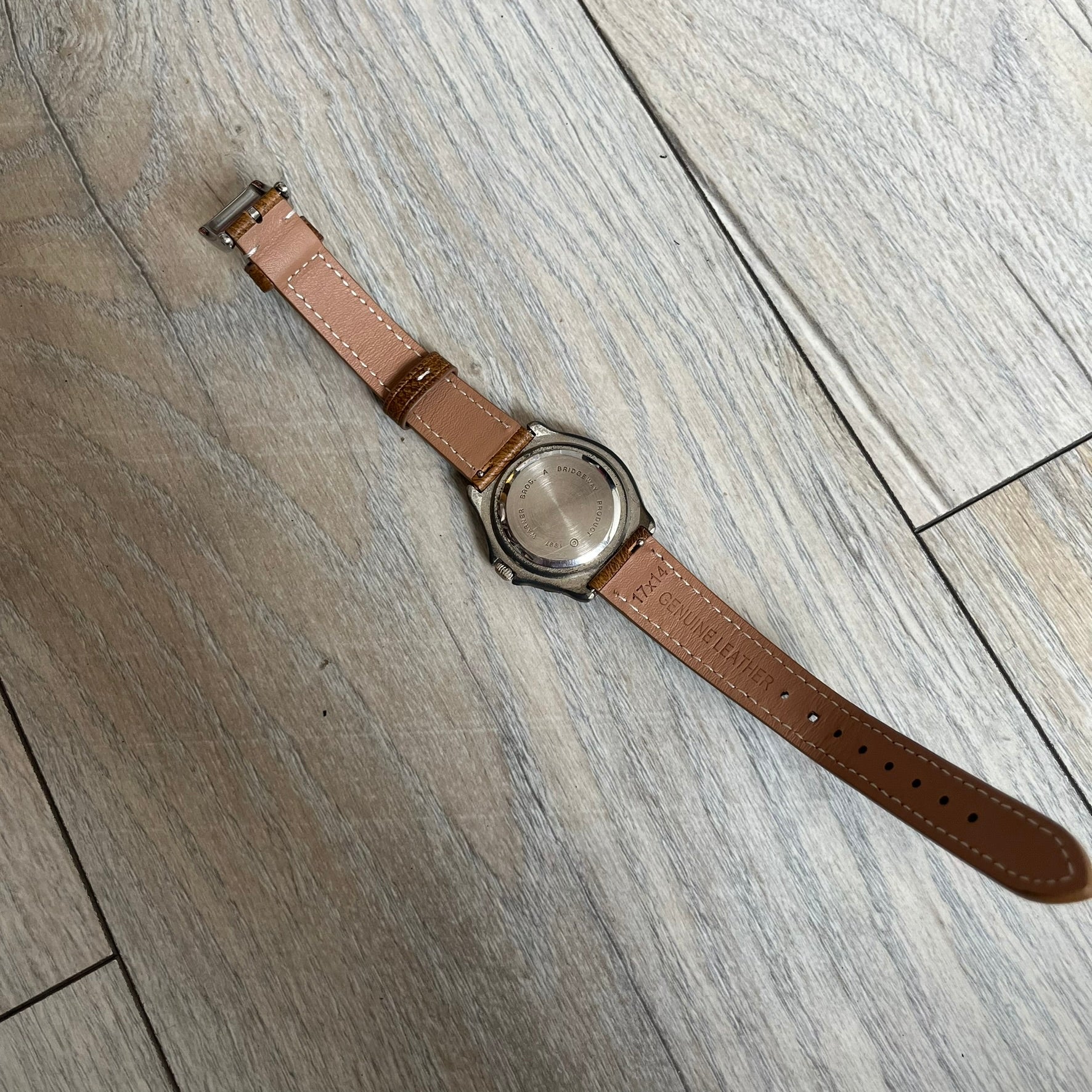 Warner Bros Tasmanian Devil 1997 Analog Watch is a stainless steel watch with a black-silver case and a fresh brown leather strap. The dial features a graphic of Taz smiling in front of a orange background. The caseback includes Warner Bros 1997 licensing