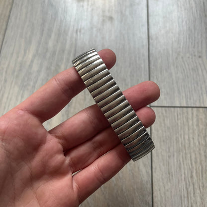 Warner Bros Tweety 1996 Analog Watch is a stainless steel watch with a stretch expansion bracelet made from connected metal links instead of a clasp. The watch features a reflective metallic dial with pink numerals and a graphic of Tweety alongside the phrase “I tawt I taw a puddy tat” in pink text. The caseback includes Warner Bros 1996 licensing.