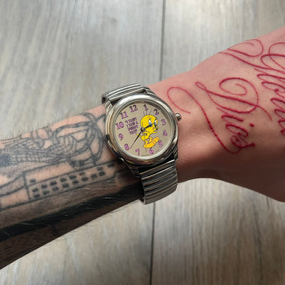 Warner Bros Tweety 1996 Analog Watch is a stainless steel watch with a stretch expansion bracelet made from connected metal links instead of a clasp. The watch features a reflective metallic dial with pink numerals and a graphic of Tweety alongside the phrase “I tawt I taw a puddy tat” in pink text. The caseback includes Warner Bros 1996 licensing.