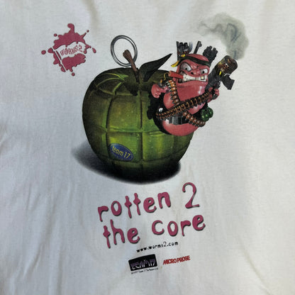 Worms 2 “Rotten 2 The Core” 1997 Tee is a white T-shirt with a front graphic of an apple styled like a grenade, with an angry worm holding a gun coming out of it. The Worms 2 logo sits to the left, and red “Rotten 2 The Core” text below the apple is followed by the website and company logos and a small 1997 licensing mark.