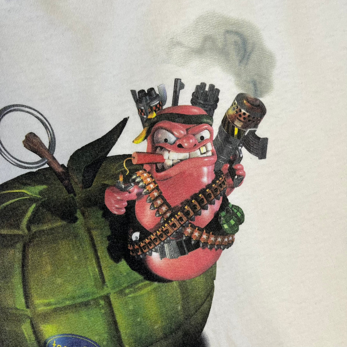 Worms 2 “Rotten 2 The Core” 1997 Tee is a white T-shirt with a front graphic of an apple styled like a grenade, with an angry worm holding a gun coming out of it. The Worms 2 logo sits to the left, and red “Rotten 2 The Core” text below the apple is followed by the website and company logos and a small 1997 licensing mark.