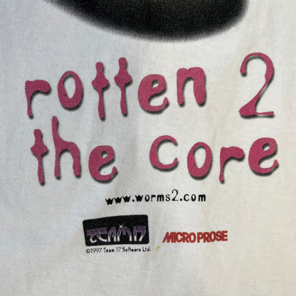 Worms 2 “Rotten 2 The Core” 1997 Tee is a white T-shirt with a front graphic of an apple styled like a grenade, with an angry worm holding a gun coming out of it. The Worms 2 logo sits to the left, and red “Rotten 2 The Core” text below the apple is followed by the website and company logos and a small 1997 licensing mark.