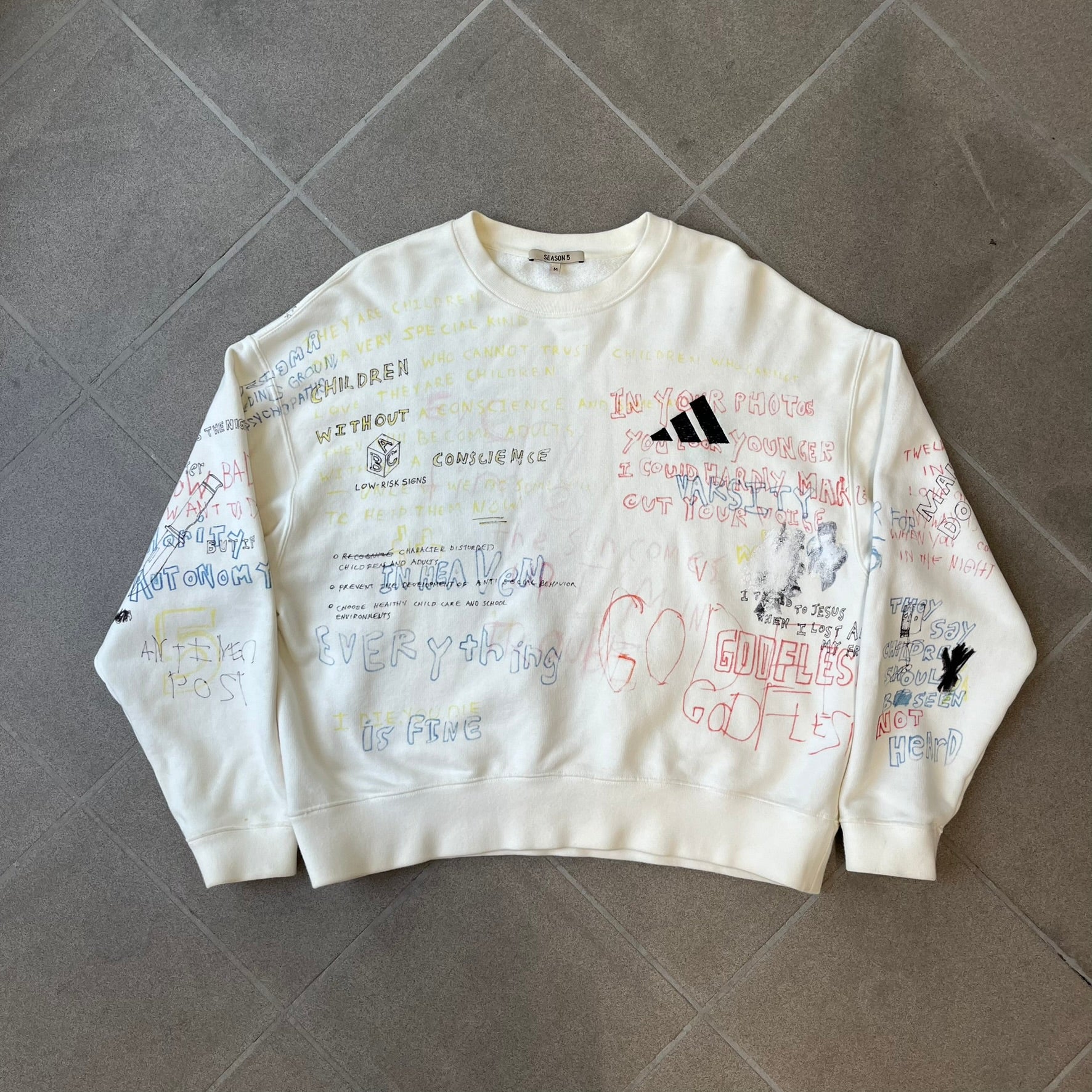Yeezy Season 5 Scribbled Adidas Crewneck by ERD features an oversized, boxy silhouette in the Arctic colorway. The 100% cotton Adidas crewneck has handwritten-style printed graphics and phrases across the garment, including a embroidered Adidas Three Stripes logo on the chest. It was made in Italy and designed by Henri Alexander Levy from Enfants Riches Déprimés.