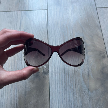 The Yves Saint Laurent 2007 Swirls 6412/S Sunglasses are an oversized model from 2007 with Category 3 sun protection. They feature oversized gradient grey lenses and burgundy (bordeaux) plastic frames, with silver-tone metal swirl details connecting the lenses to the temples. The temples are finished with a metal Yves Saint Laurent logo integrated into the swirl hardware. Made in Italy, with all original markings located on the inside. They come with a white leather YSL case.