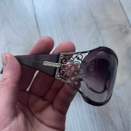 The Yves Saint Laurent 2007 Swirls 6412/S Sunglasses are an oversized model from 2007 with Category 3 sun protection. They feature oversized gradient grey lenses and burgundy (bordeaux) plastic frames, with silver-tone metal swirl details connecting the lenses to the temples. The temples are finished with a metal Yves Saint Laurent logo integrated into the swirl hardware. Made in Italy, with all original markings located on the inside. They come with a white leather YSL case.