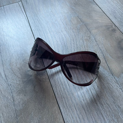 The Yves Saint Laurent 2007 Swirls 6412/S Sunglasses are an oversized model from 2007 with Category 3 sun protection. They feature oversized gradient grey lenses and burgundy (bordeaux) plastic frames, with silver-tone metal swirl details connecting the lenses to the temples. The temples are finished with a metal Yves Saint Laurent logo integrated into the swirl hardware. Made in Italy, with all original markings located on the inside. They come with a white leather YSL case.