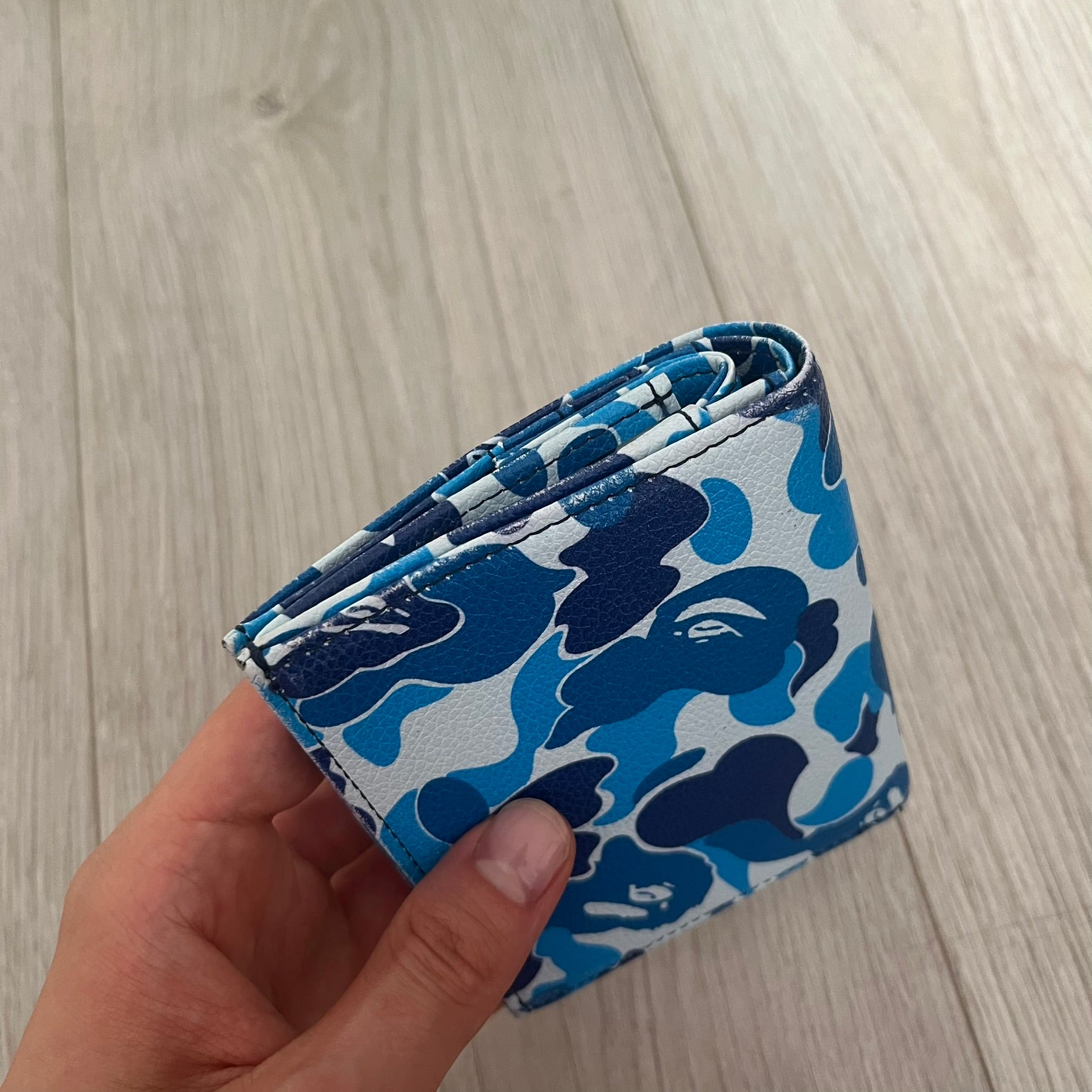 Blue camouflage wallet held by a hand on a light wooden surface