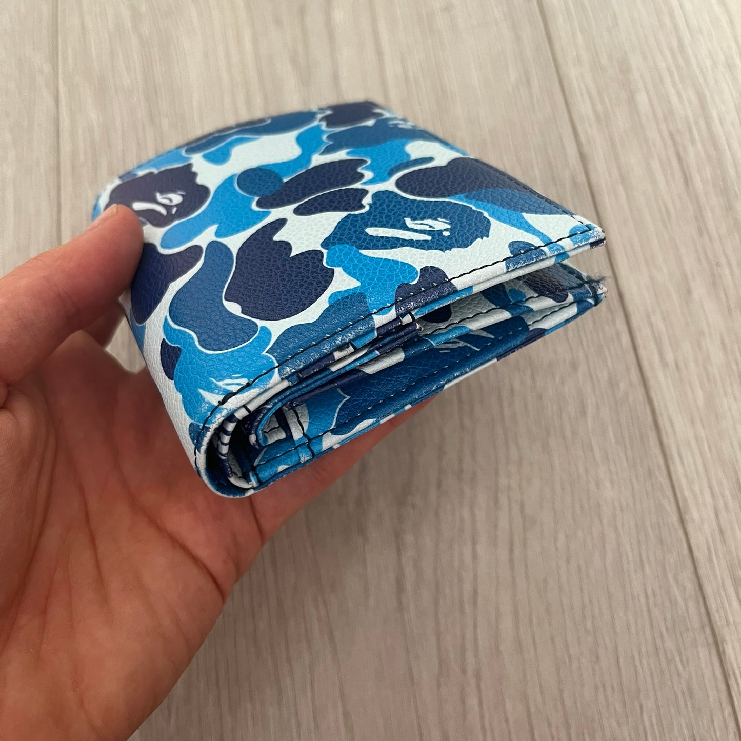Hand holding a blue camouflage-patterned pouch against a light wooden background