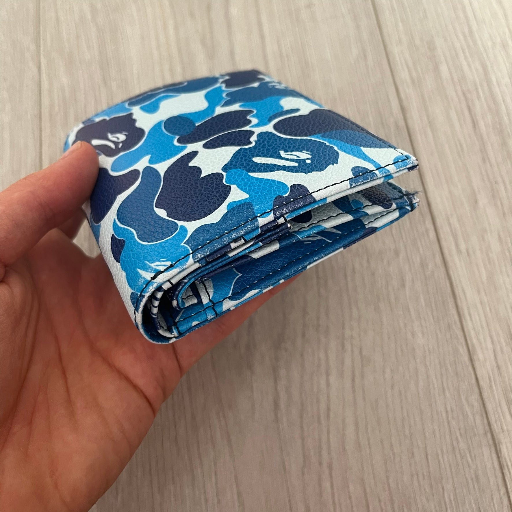 Hand holding a blue camouflage-patterned pouch against a light wooden background