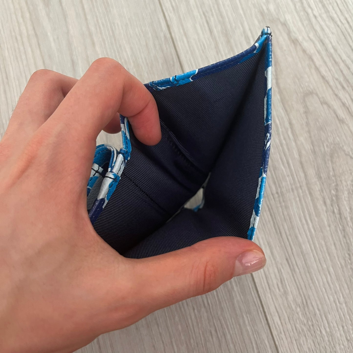Hand holding a navy blue fabric with blue floral pattern on a wooden surface