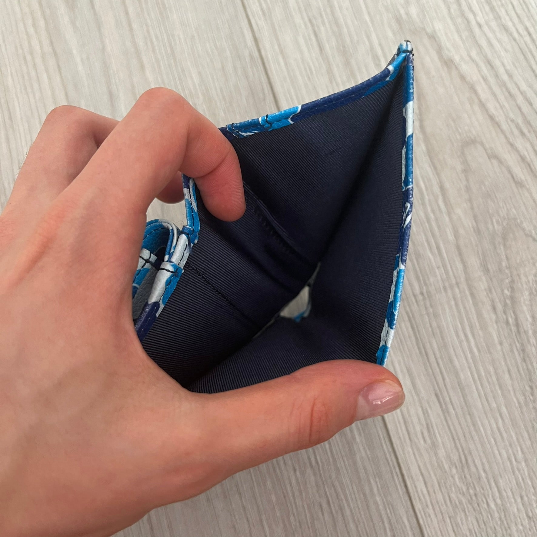 Hand holding a navy blue fabric with blue floral pattern on a wooden surface