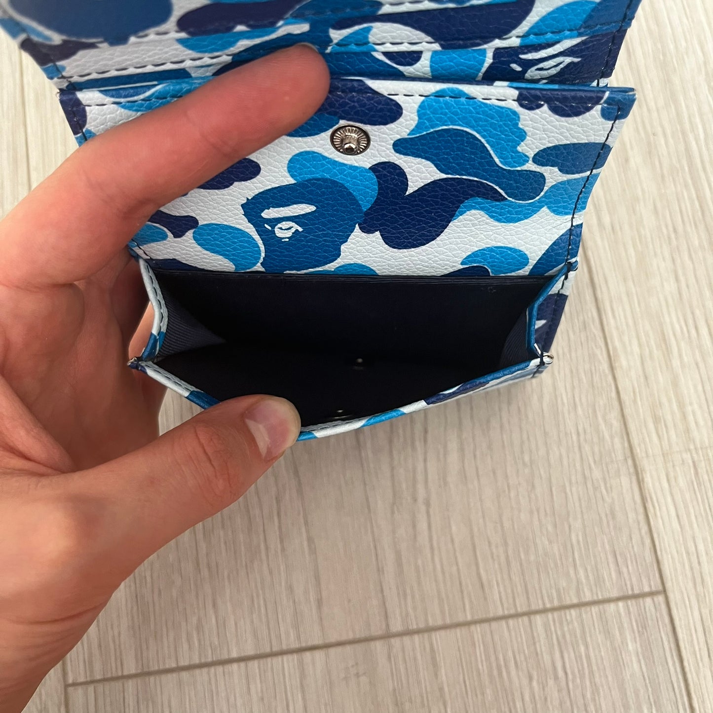 Hand holding a blue and white floral patterned wallet on a light wooden surface