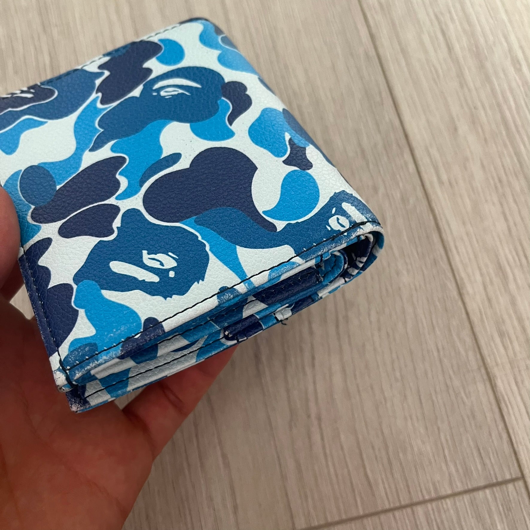 Blue camouflage wallet held by a hand on a wooden surface