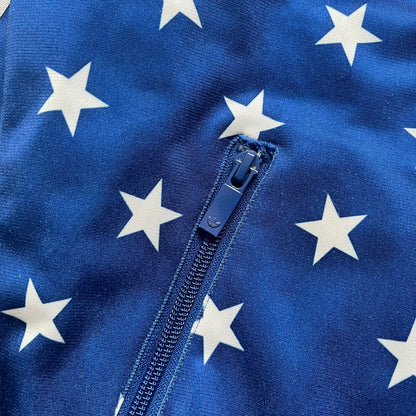 Adidas Originals Stars Blue Track Jacket is a blue zip-up track jacket featuring an all-over white star print. It includes white Adidas three-stripes along the sleeves and a small Adidas Originals patch on the chest. The design closely resembles star-pattern track jacket by Jeremy Scott for Adidas Originals.