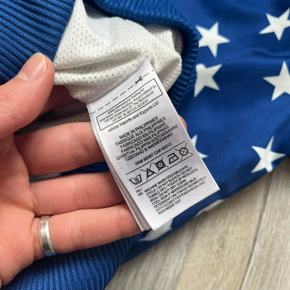 Adidas Originals Stars Blue Track Jacket is a blue zip-up track jacket featuring an all-over white star print. It includes white Adidas three-stripes along the sleeves and a small Adidas Originals patch on the chest. The design closely resembles star-pattern track jacket by Jeremy Scott for Adidas Originals.