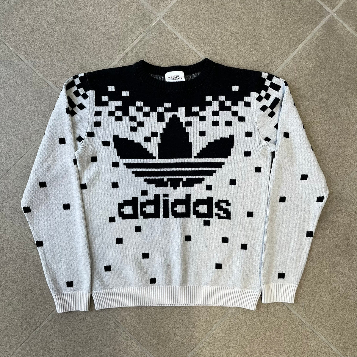 adidas Originals by Jeremy Scott 2013 Pixel Sweater features a white construction with a black upper section that transitions into a pixelated pattern, with black pixels appearing to fall down across the white body. The same pixelated design continues on the back, while the front has a pixelated adidas Trefoil logo. Part of the SS13 collection.
