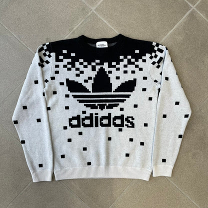 adidas Originals by Jeremy Scott 2013 Pixel Sweater features a white construction with a black upper section that transitions into a pixelated pattern, with black pixels appearing to fall down across the white body. The same pixelated design continues on the back, while the front has a pixelated adidas Trefoil logo. Part of the SS13 collection.

