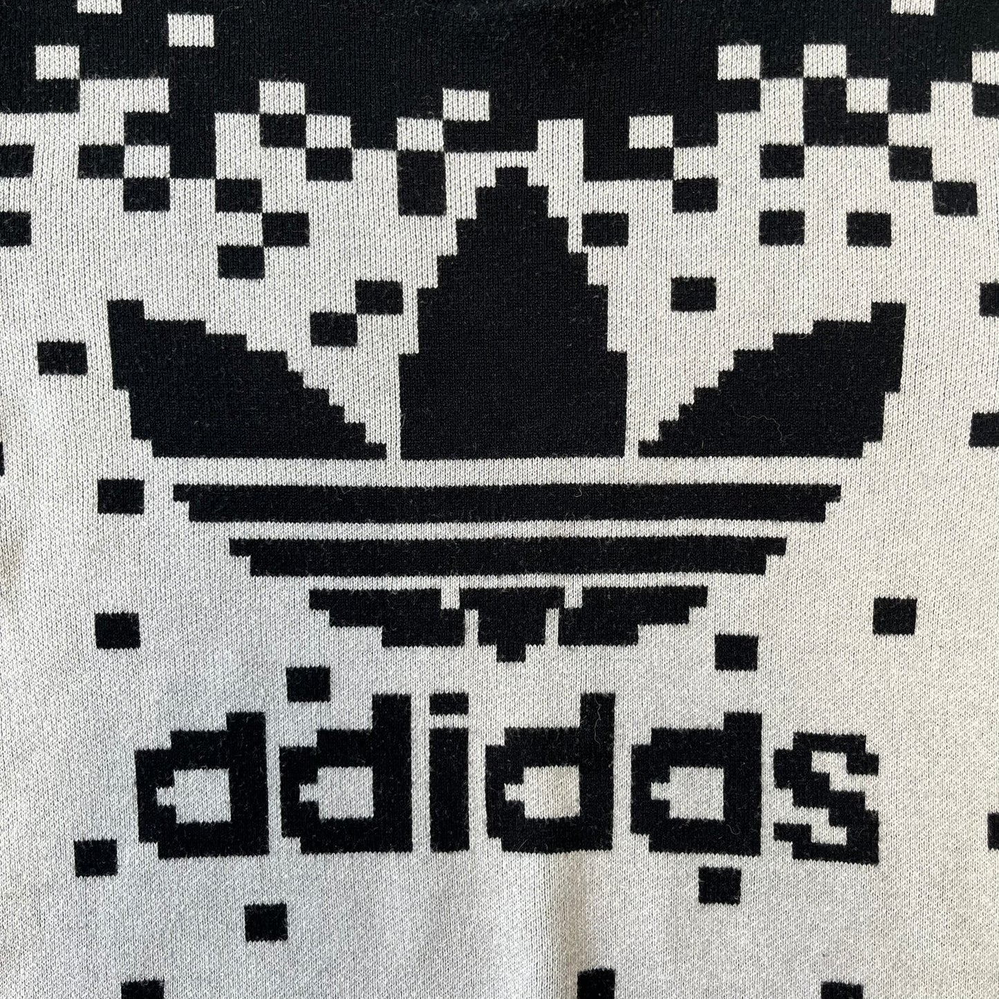 adidas Originals by Jeremy Scott 2013 Pixel Sweater features a white construction with a black upper section that transitions into a pixelated pattern, with black pixels appearing to fall down across the white body. The same pixelated design continues on the back, while the front has a pixelated adidas Trefoil logo. Part of the SS13 collection.

