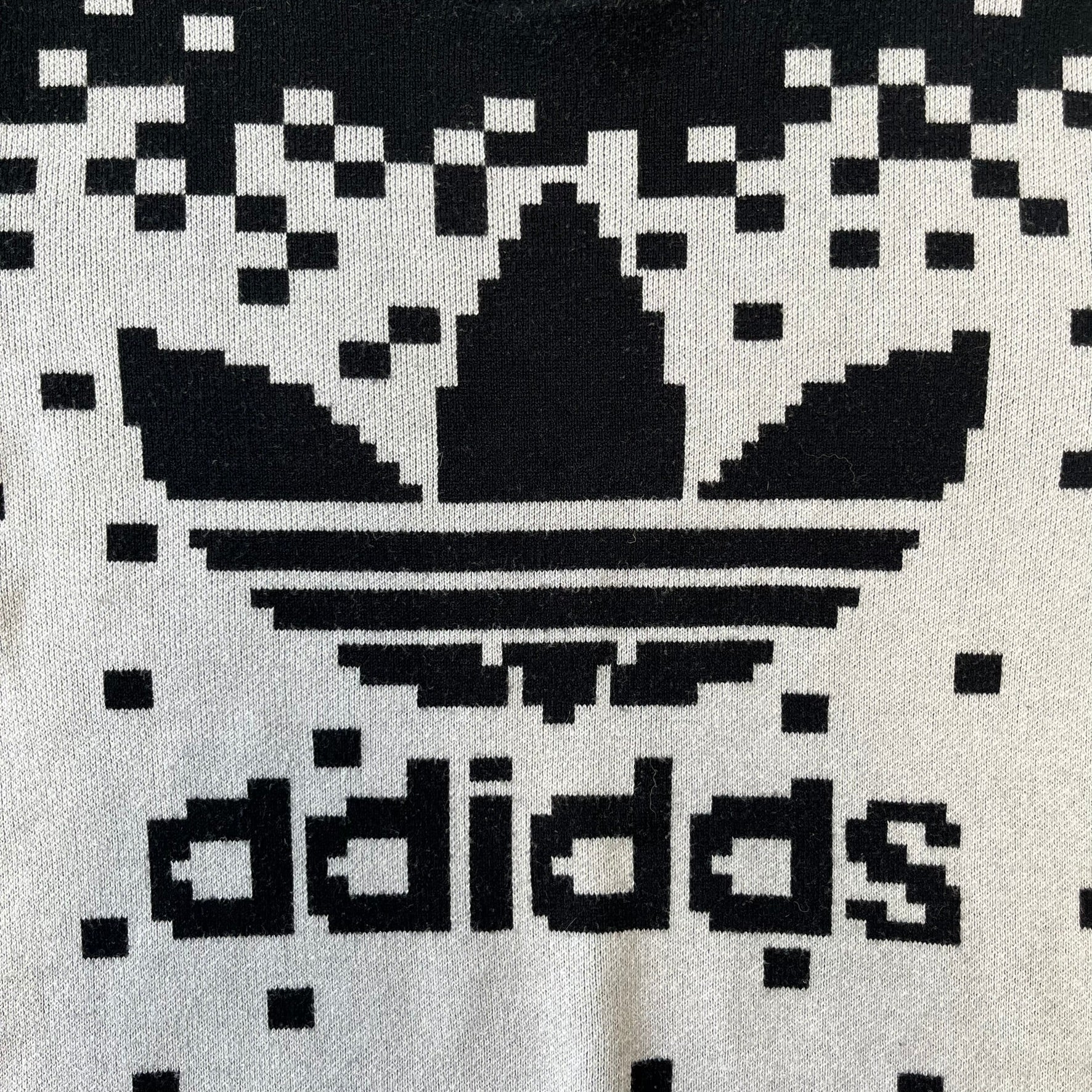 adidas Originals by Jeremy Scott 2013 Pixel Sweater features a white construction with a black upper section that transitions into a pixelated pattern, with black pixels appearing to fall down across the white body. The same pixelated design continues on the back, while the front has a pixelated adidas Trefoil logo. Part of the SS13 collection.
