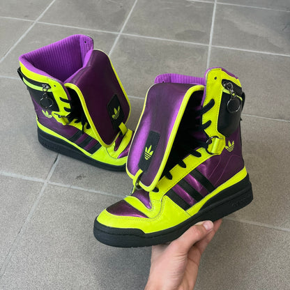 adidas Originals by Jeremy Scott 2014 JS Tall Boy Summer Sneakers feature a yellow and metallic purple high-top construction with a patent-effect synthetic upper. The design has an oversized foldable tongue, ribbed lining, ankle zipper, and abrasion-resistant rubber sole. Part of the adidas Originals by Jeremy Scott SS14 collection.
