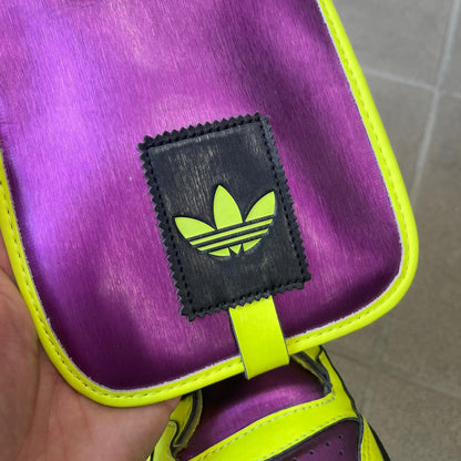 adidas Originals by Jeremy Scott 2014 JS Tall Boy Summer Sneakers feature a yellow and metallic purple high-top construction with a patent-effect synthetic upper. The design has an oversized foldable tongue, ribbed lining, ankle zipper, and abrasion-resistant rubber sole. Part of the adidas Originals by Jeremy Scott SS14 collection.
