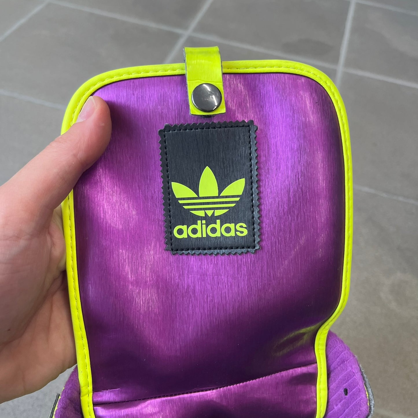 adidas Originals by Jeremy Scott 2014 JS Tall Boy Summer Sneakers feature a yellow and metallic purple high-top construction with a patent-effect synthetic upper. The design has an oversized foldable tongue, ribbed lining, ankle zipper, and abrasion-resistant rubber sole. Part of the adidas Originals by Jeremy Scott SS14 collection.
