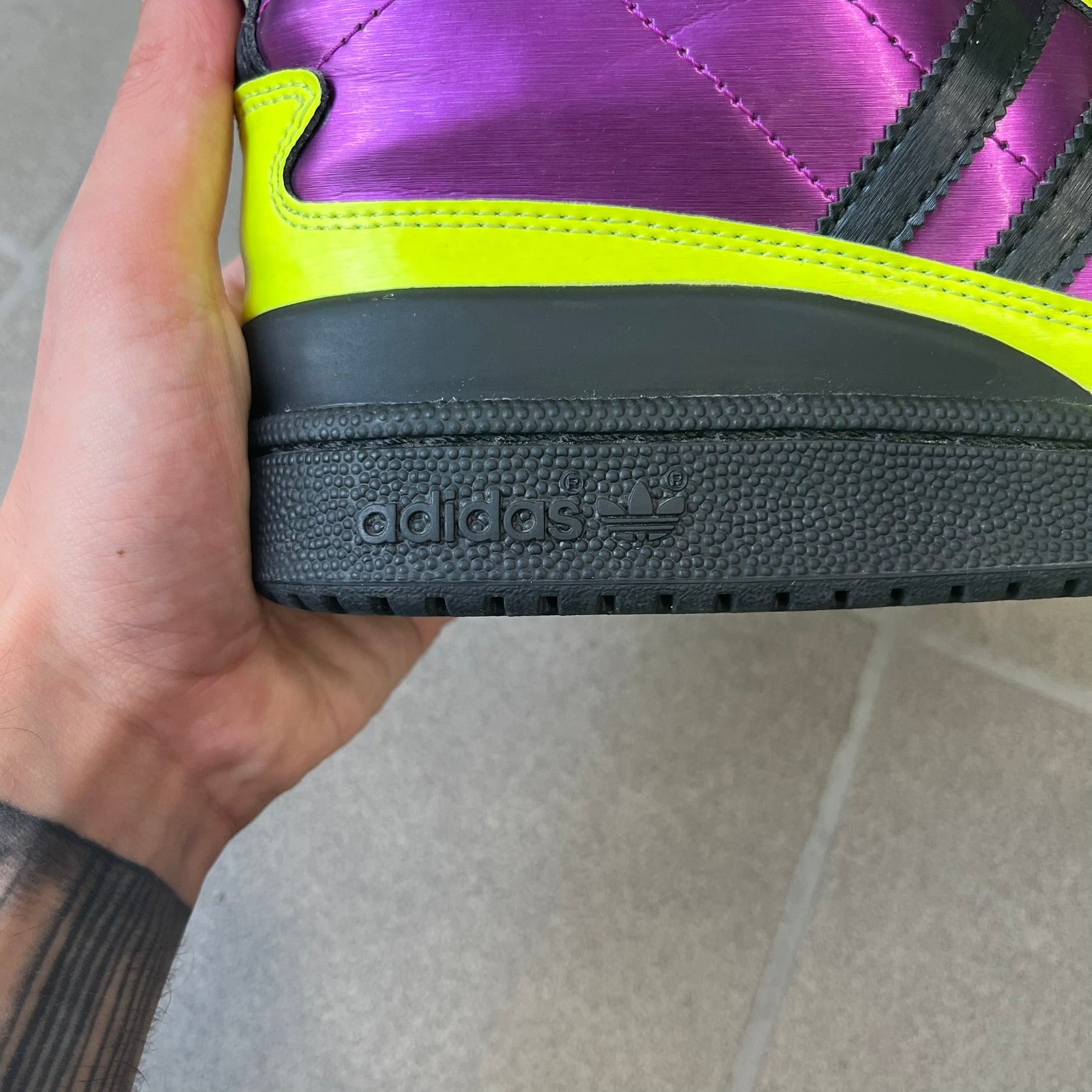 adidas Originals by Jeremy Scott 2014 JS Tall Boy Summer Sneakers feature a yellow and metallic purple high-top construction with a patent-effect synthetic upper. The design has an oversized foldable tongue, ribbed lining, ankle zipper, and abrasion-resistant rubber sole. Part of the adidas Originals by Jeremy Scott SS14 collection.
