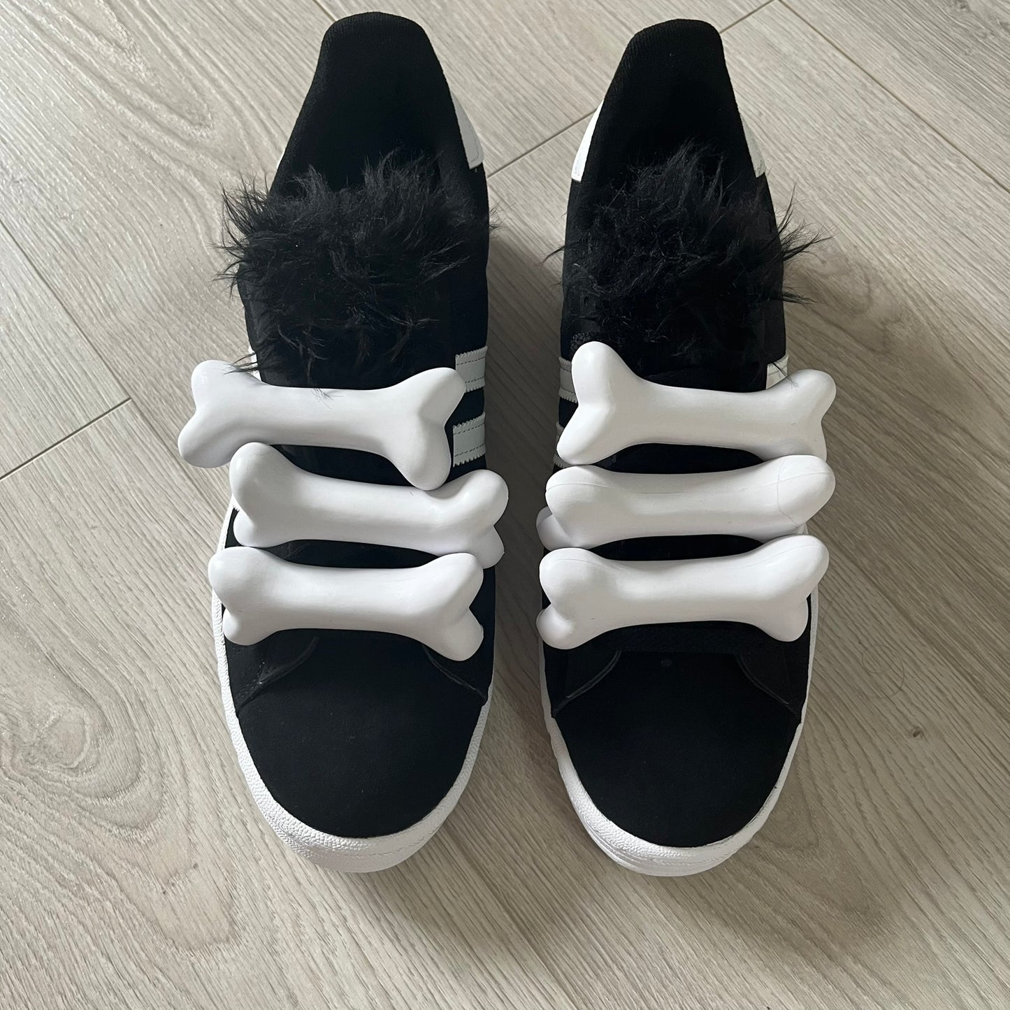 jeremy scott’s take on the adidas campus 80s includes black leather, serrated stripes, and unique faux fur tongues. detachable white bones on the laces add a customizable, standout touch. this 2023 release balances classic style with avant-garde details.