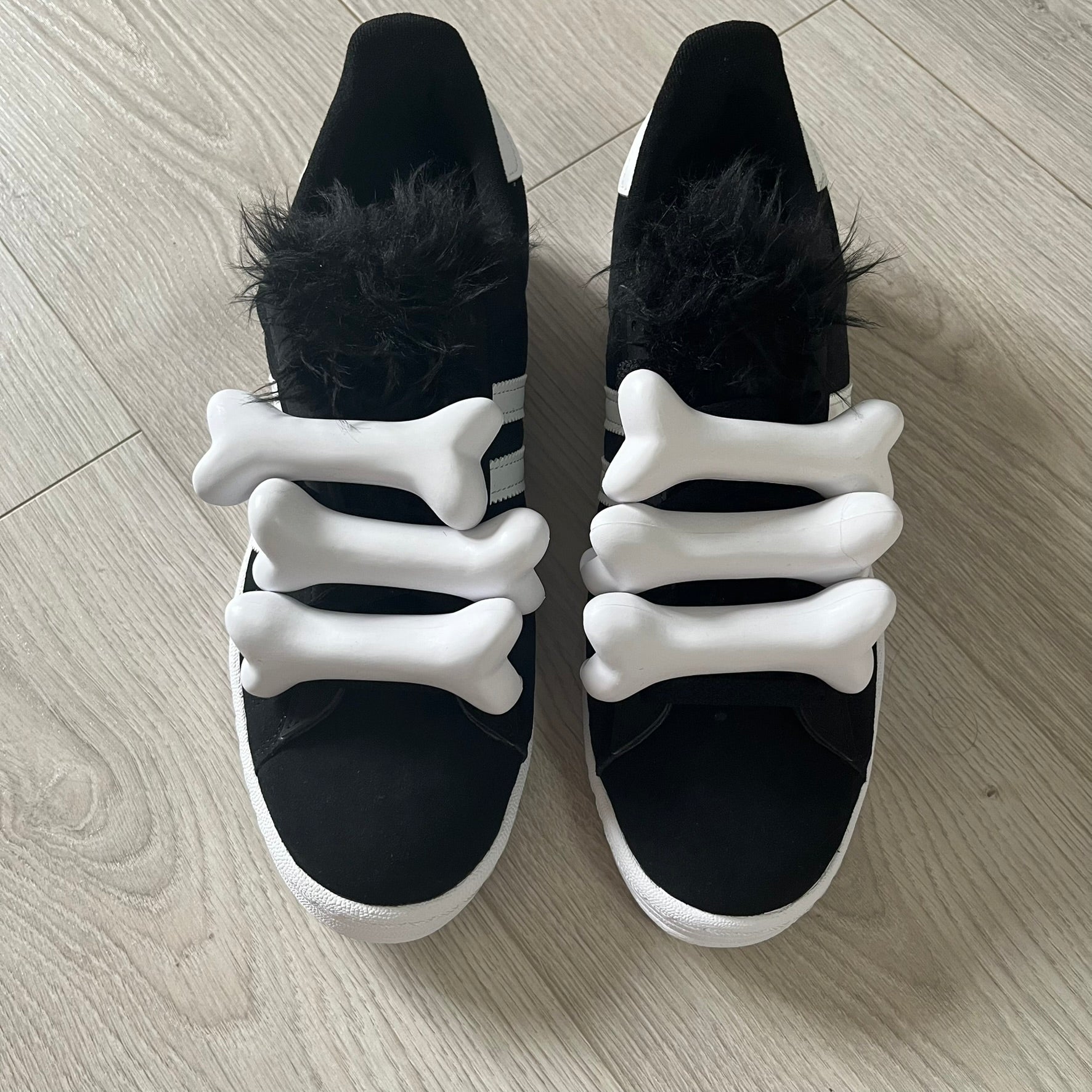 jeremy scott’s take on the adidas campus 80s includes black leather, serrated stripes, and unique faux fur tongues. detachable white bones on the laces add a customizable, standout touch. this 2023 release balances classic style with avant-garde details.