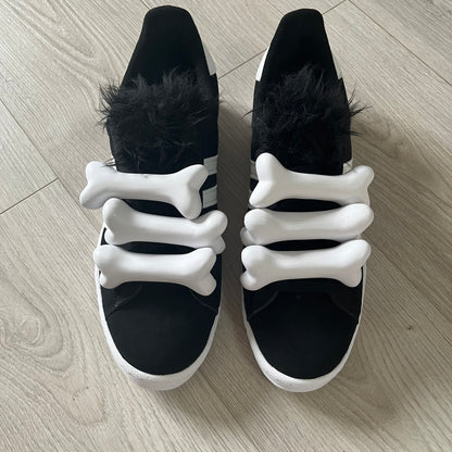 jeremy scott’s take on the adidas campus 80s includes black leather, serrated stripes, and unique faux fur tongues. detachable white bones on the laces add a customizable, standout touch. this 2023 release balances classic style with avant-garde details.