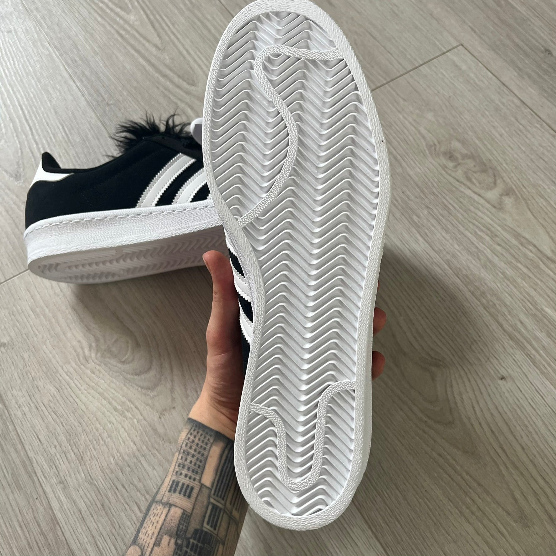 jeremy scott’s take on the adidas campus 80s includes black leather, serrated stripes, and unique faux fur tongues. detachable white bones on the laces add a customizable, standout touch. this 2023 release balances classic style with avant-garde details.