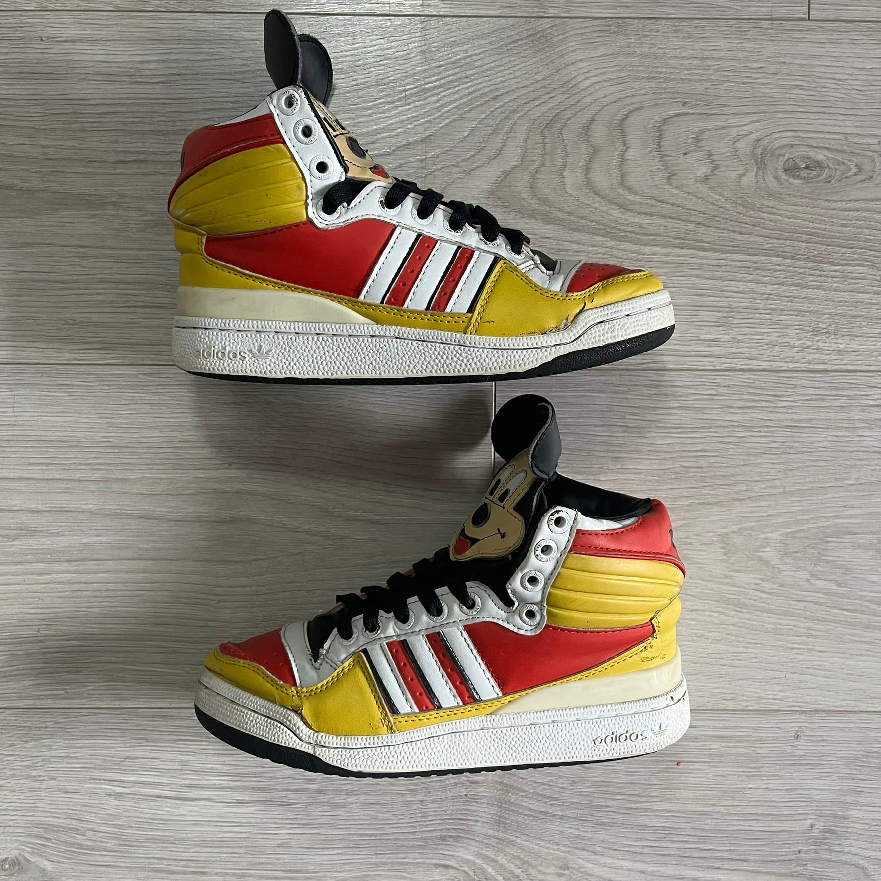 Pair of Adidas sneakers with a colorful design on a wooden floor.