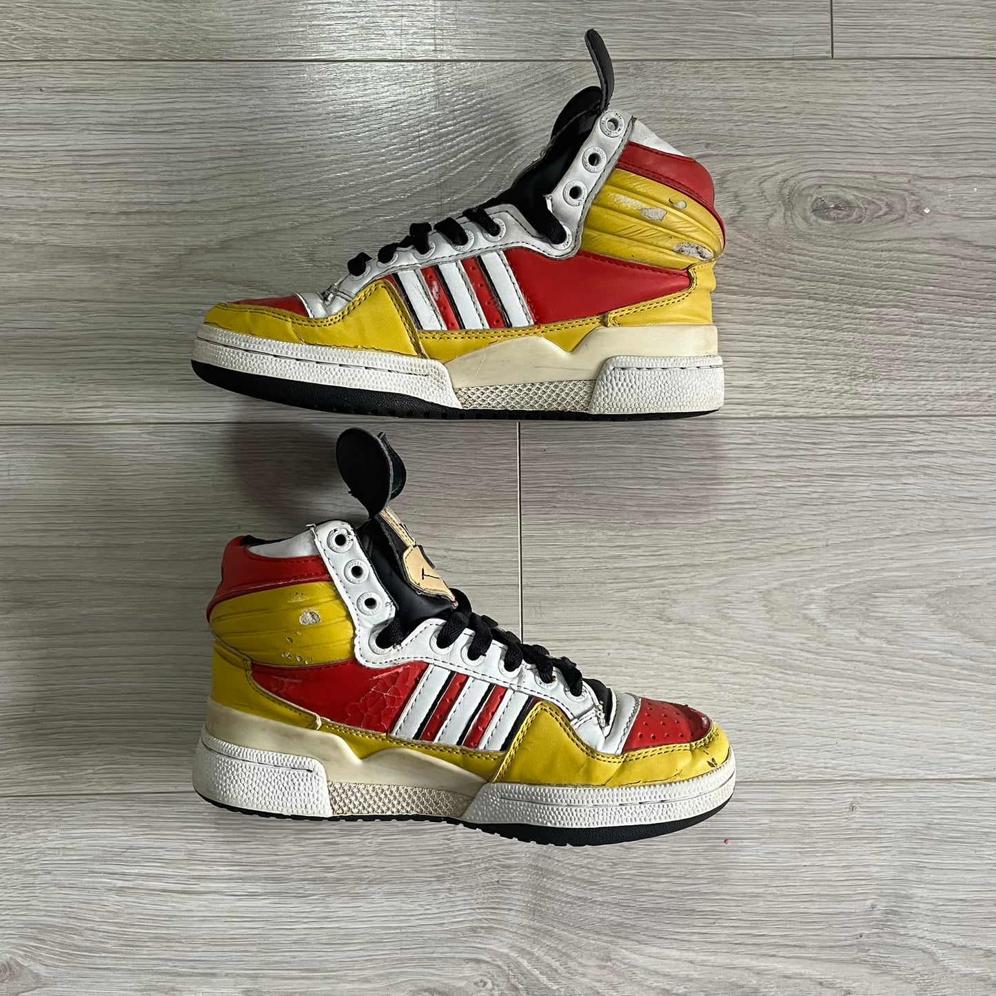 Pair of red, yellow, and white sneakers with black accents on a wooden floor.