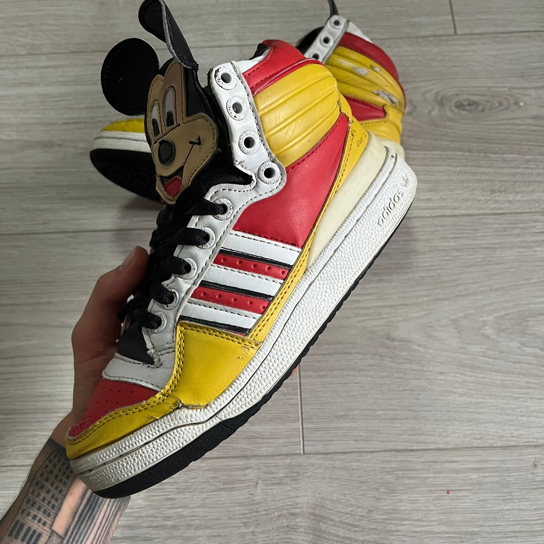 Colorful sneaker with cartoon character design held by a hand on a wooden floor.