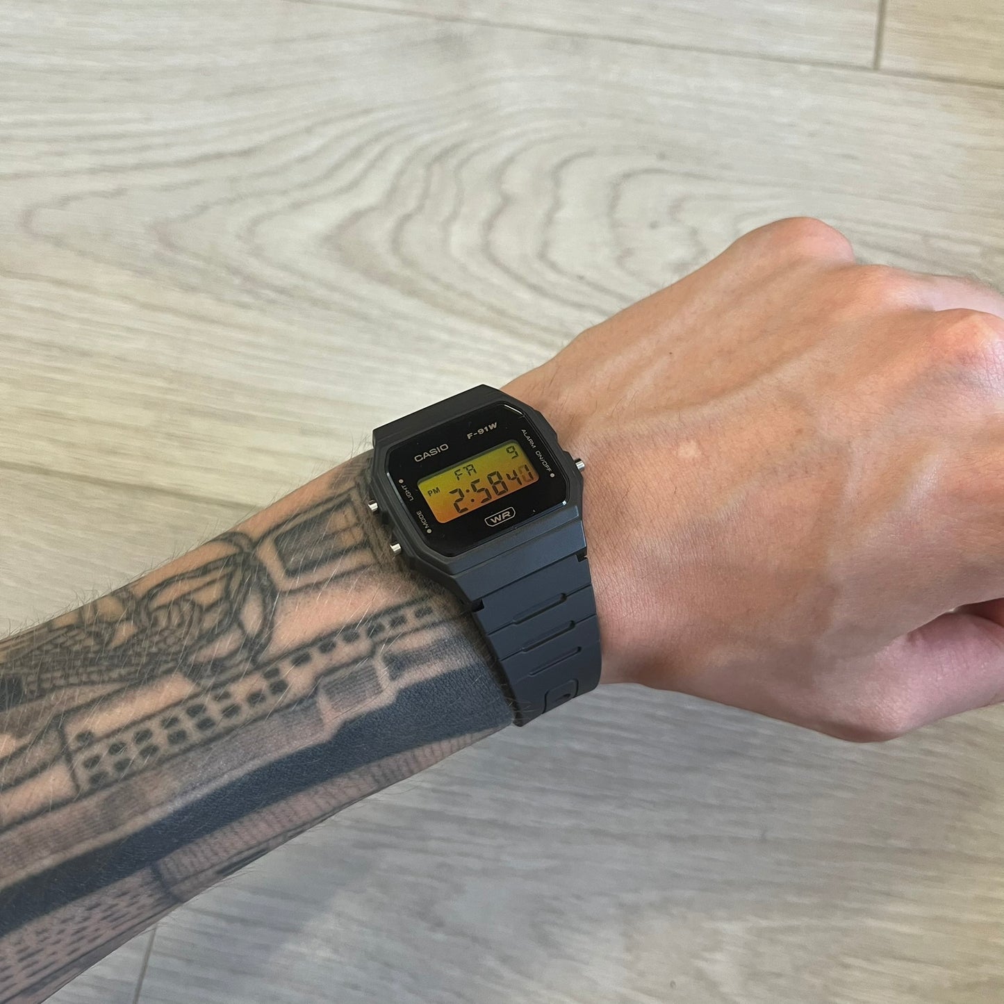 Person wearing a black digital watch on a light wood surface