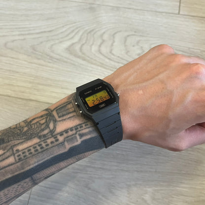 Person wearing a black digital watch on a light wood surface