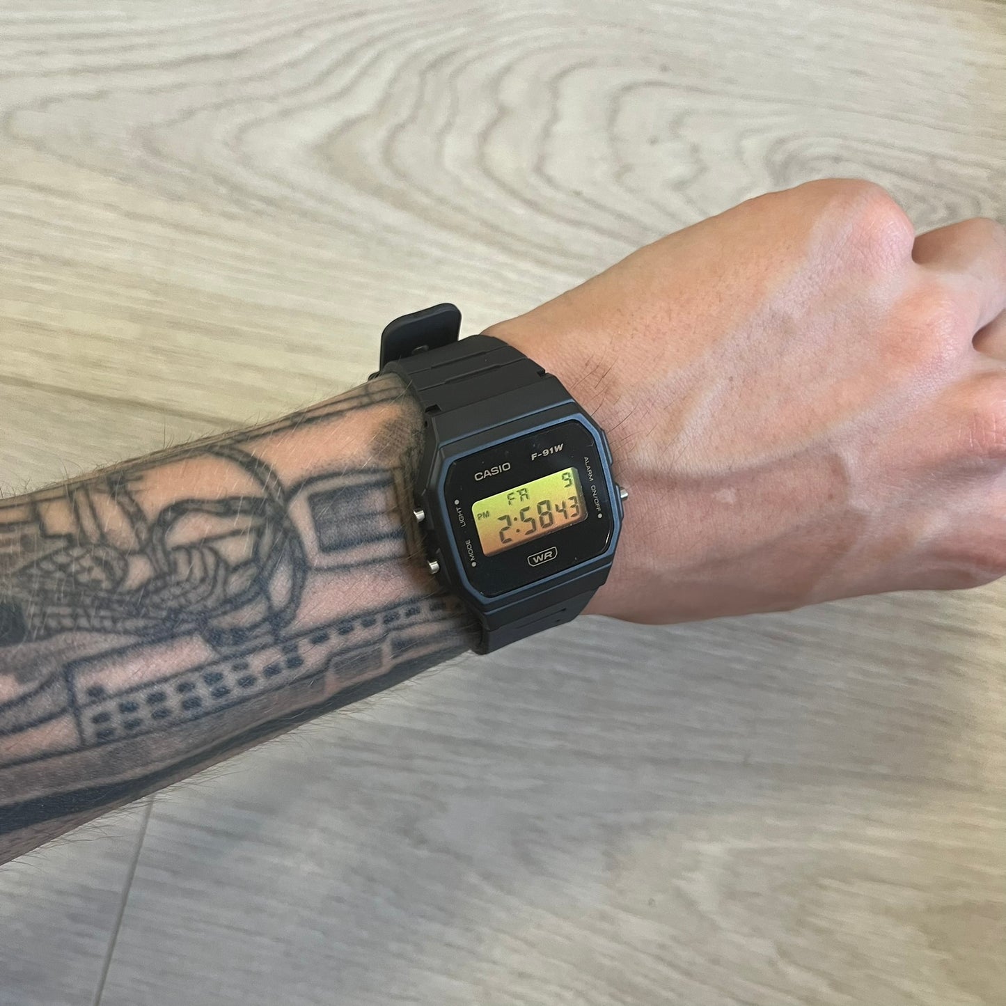 Black Casio digital watch on a wrist with tattoos, on a wooden floor background