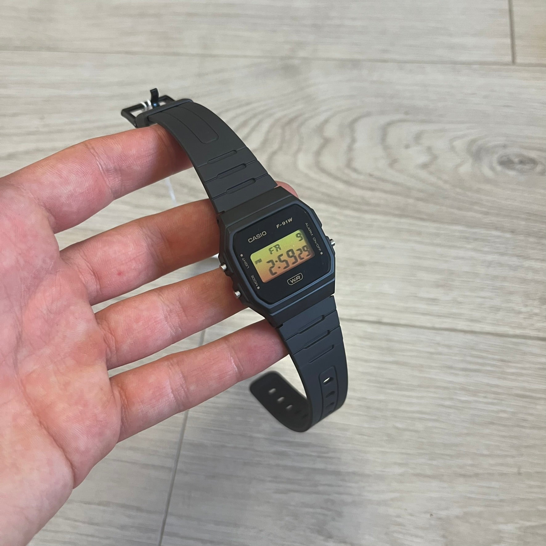 Black Casio digital watch held in a hand on a wooden surface
