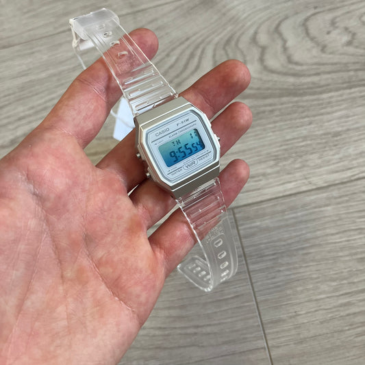 Digital watch with clear strap held in a hand on a wooden surface