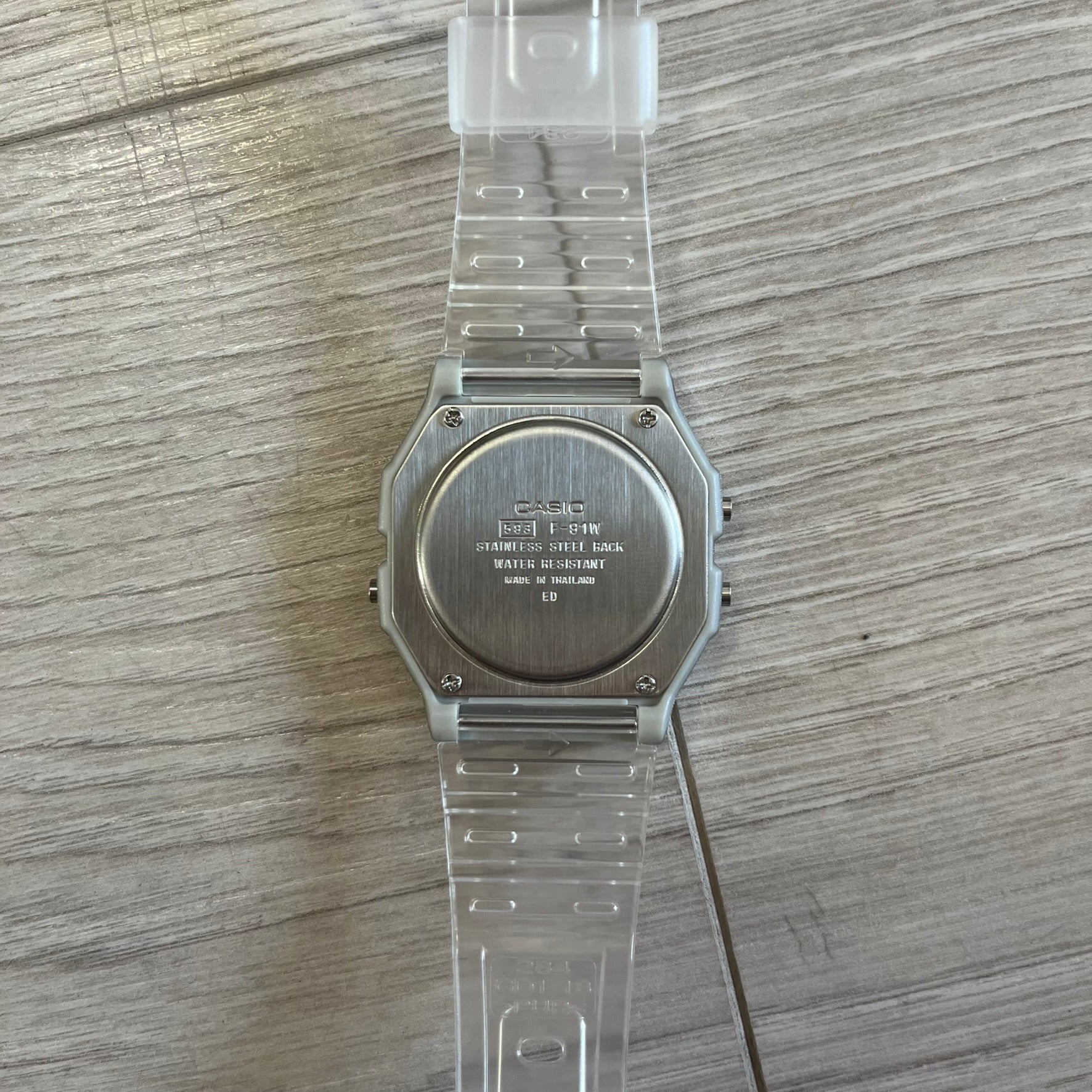 Clear plastic watch with metal back on a wooden surface