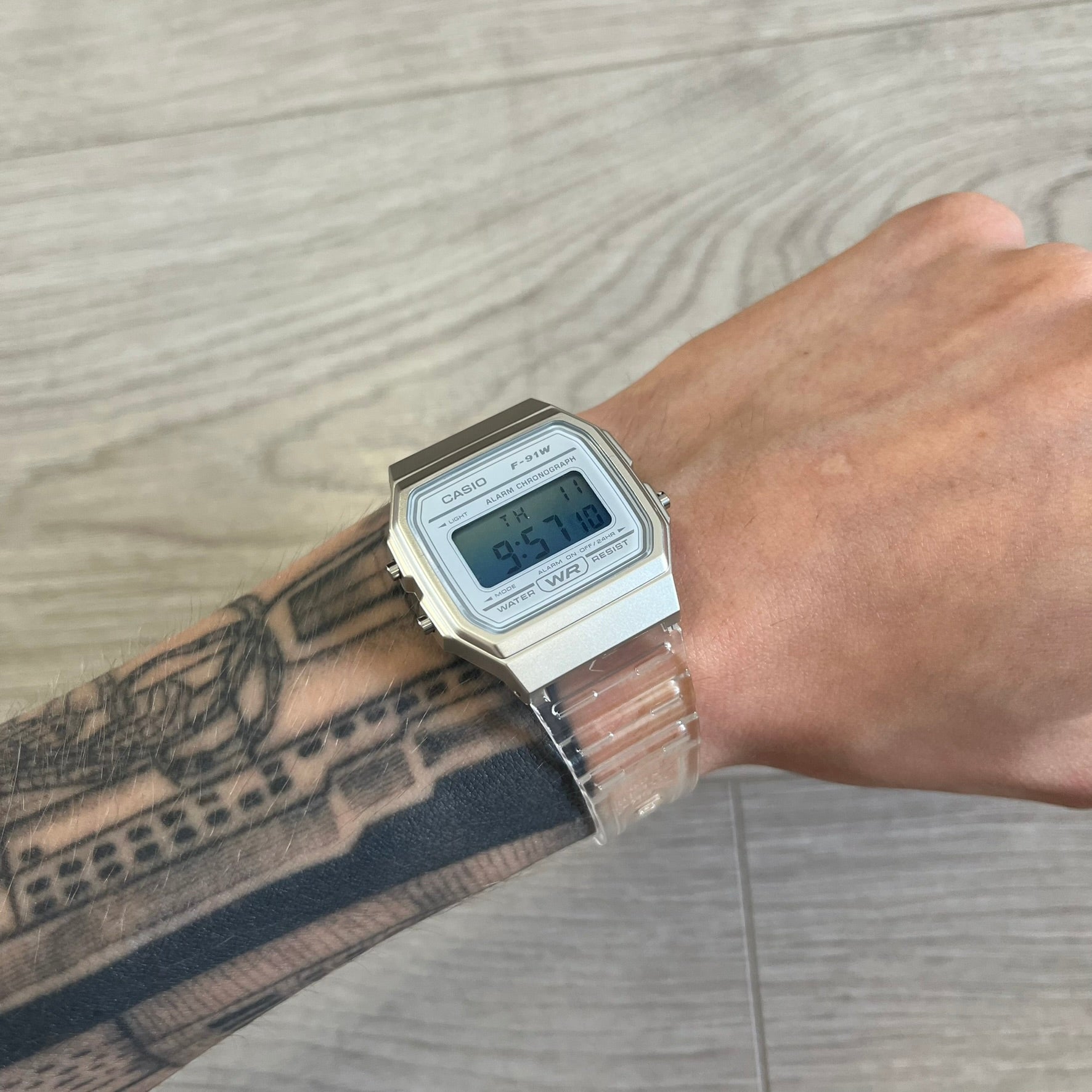 Digital watch on a wrist with a tattooed arm against a wooden background