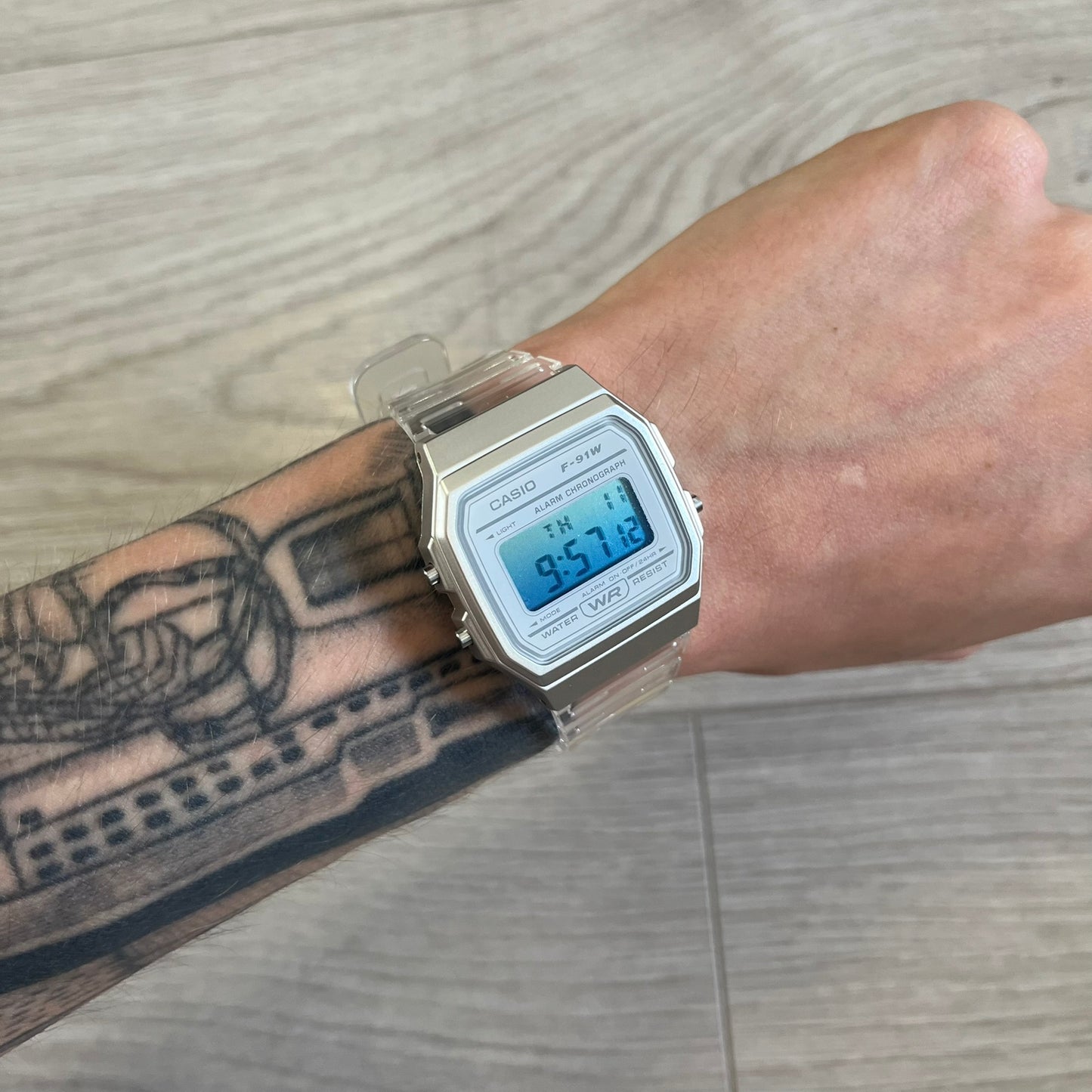 Digital watch on a wrist with a tattooed arm, wooden floor background